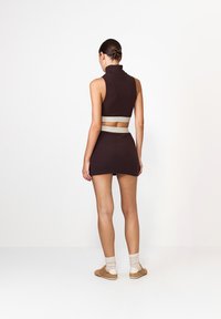 Hnědý bezrukávový crop top s vysokým límcem a odpovídající mini sukni. Obsahuje texturovanou látku a pás z světlé barvy.