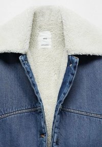 Veste en denim avec une doublure douce en sherpa crème. Comprend un col classique, un extérieur en denim bleu et des boutons-pression métalliques. L'étiquette indique « MNG ».