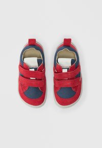 Chaussures rouges et bleu marine avec des brides auto-agrippantes, dotées d'une empeigne en daim, de panneaux en mesh, d'un intérieur rembourré et d'une semelle en caoutchouc.