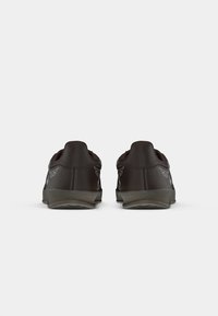 Zwarte sneakers met een gladde textuur, gebogen ontwerp en grijze rubberen zolen. Opvallende details aan de achterkant bevatten subtiele grafische accenten.
