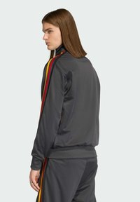 Grijze trainingsjack met geribde manchetten, hoge kraag en rode en gele zijstrepen. Gladde, elegante stof met een aansluitende silhouet.