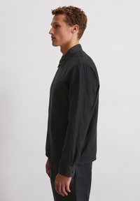 Black linen shirt with long sleeves, button-up collar, single chest pocket, and subtle texture. Styled with matching pants.
