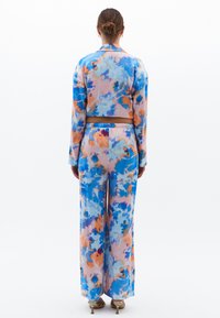 Ensemble deux pièces à imprimé floral comprenant une veste courte et un pantalon large. Les couleurs incluent le bleu, le rose et l'orange avec une texture lisse.
