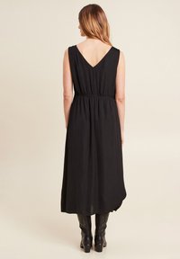 Zwart mouwloos maxi jurk met een V-hals aan de achterkant, gathered taille en een vloeiende rok. Soepele structuur, casual ontwerp en enkel-lange silhouet.
