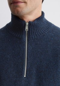 Marineblauer Reißverschluss-Pullover mit hohem Kragen, der eine gerippte Textur und subtile Sprenkel aufweist. Metallreißverschluss am Hals.