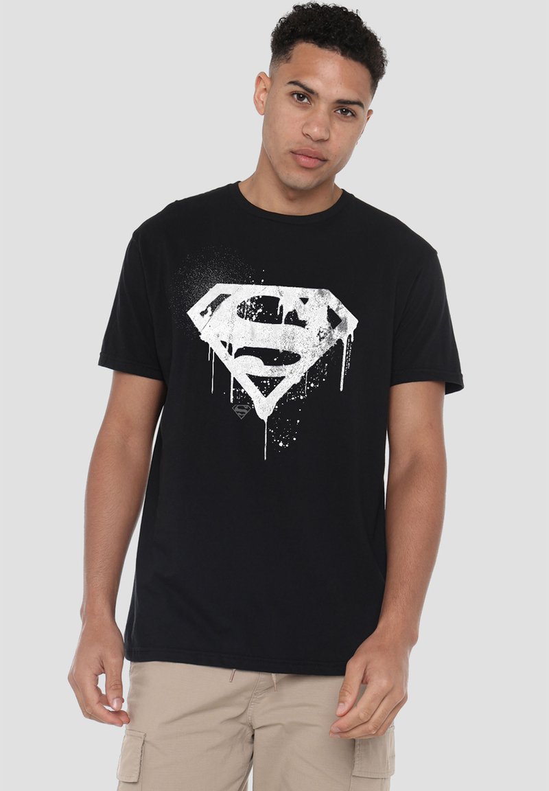 Black cotton t-shirt featuring a white splattered Superman logo design at the center, short sleeves, and a round neckline.