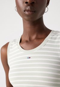 Heled roheline ribaga tank-ülemine, millel on valged triibud ja väikene logo detail punases, valges ja sinises värvis rinnapiirkonnas.
