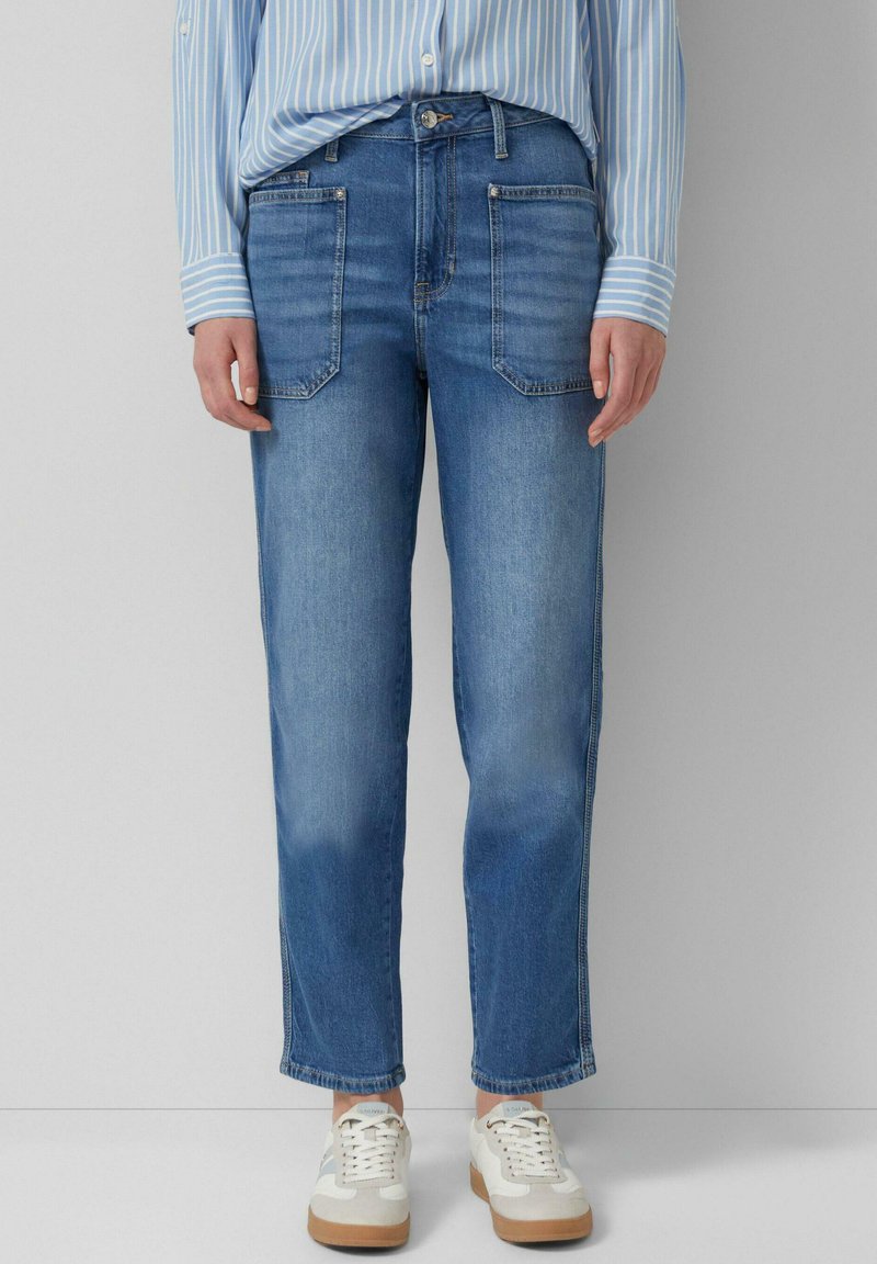 Personne portant un jean droit bleu avec de grandes poches avant, une chemise rayée bleue et blanche rentrée, et des baskets blanches.