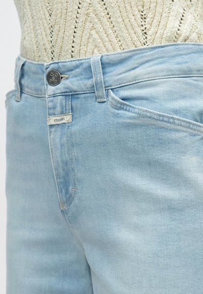 Ανοιχτό μπλε τζιν με κλασική εφαρμογή, διαθέτοντας κλείσιμο με κουμπί, μπροστινές τσέπες και μια μικρή ετικέτα "CLOSED" στην τσέπη.