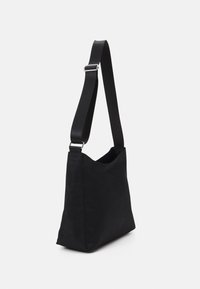 Černá látková taška přes rameno s hladkou texturou, minimalistickým designem, nastavitelným popruhem a otevřeným vrškem pro snadný přístup.