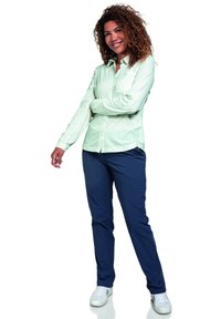 Camisa de manga larga en menta claro con botones y cuello puntiagudo, combinada con pantalones azul oscuro. Usada con zapatillas blancas; textura suave en general.
