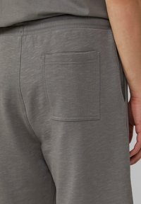 Graue Sweatpants aus einem weichen, strukturierten Stoff, ausgestattet mit einem elastischen Bund und einer aufgesetzten Tasche auf der Rückseite.
