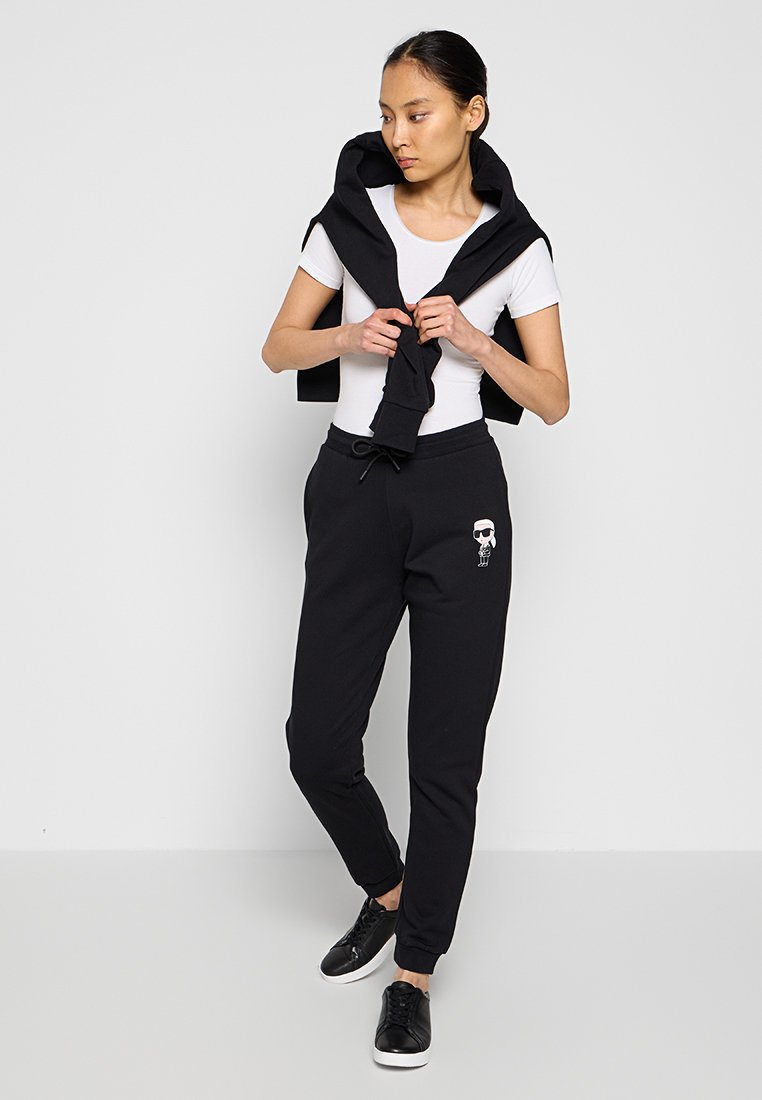 Pantalons de jogging noirs avec des poignets élastiques, une taille à cordon et un design graphique. Associés à un haut blanc ajusté et des baskets noires.