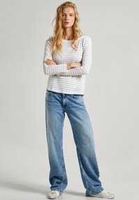 Camicia a maniche lunghe a righe in grigio chiaro e bianco, abbinata a jeans larghi di colore azzurro chiaro e sneakers bianche. Design semplice e dal taglio rilassato.