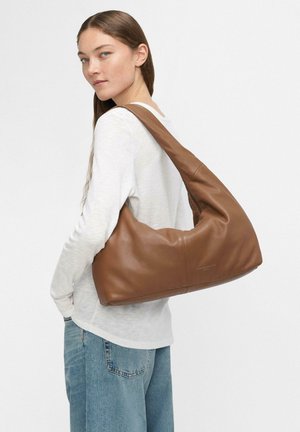 Borsa a tracolla in pelle marrone con un design morbido e rilassato. Presenta una forma curva e un branding discreto, abbinata a una parte superiore chiara e jeans.