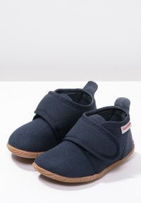 Marineblauwe stoffen schoenen met een klittenbandsluiting, ronde neus, zachte textuur en een lichtbruine rubberen zool met groeven. Logo op de zijkant.