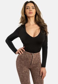 Body nero a maniche lunghe con scollatura a V profonda, abbinato a pantaloni marroni a vita alta e texture, con zip frontale e motivi sottili.