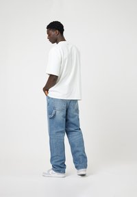 T-shirt blanche oversize, jeans bleus à coupe décontractée et sneakers blanches. Style décontracté avec un minimum de détails et une silhouette ample.