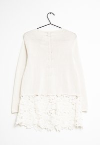 Kerman neulejakku pitsireunuksella. Yläosassa on teksturoitu kuvio; alaosa koostuu kukkakehyksestä, jossa on aaltoilevat reunat. Ripustettu mustalle koukulle.