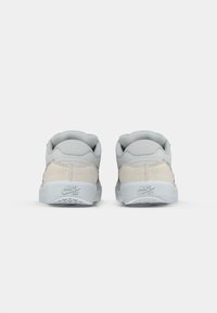 Nike SB tenisice s mekim gornjim dijelom od sive i bež zamjene, zaobljenim petama i mekanim jastučićem. Sadrži logo na peti i teksturiranu potplatu.