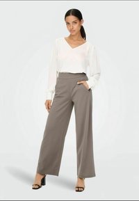 Biała bluzka z długim rękawem i dekoltem w serek w połączeniu z szarymi, szerokimi spodniami z wysokim stanem i bocznymi kieszeniami. Całość uzupełniają czarne szpilki.