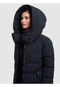 Giacca a vento nera con un grande cappuccio, texture trapuntata, zip frontale e tasche laterali con chiusura a zip.