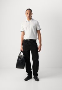 Weißes Poloshirt mit marineblauem Besatz, schwarze Hose und schwarze Ledertasche. Glatte Textur, klassischer Schnitt und dezentes Logo-Detail auf dem Shirt.