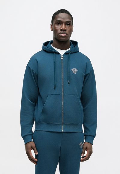 Morská modrozelená mikina na zips z mäkkého materiálu, s klokankovým vreckom a kapucňou so šnúrkou. Vyšívané logo tigra na ľavej strane hrude.