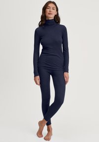 Marineblauwe coltrui en bijpassende legging, gemaakt van een zachte, rekbare stof. Het kledingstuk heeft een aansluitend ontwerp met lange mouwen en naden.