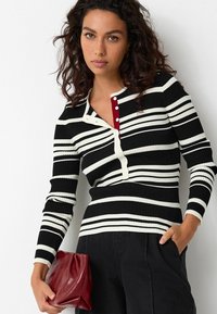 Černobílý pruhovaný žebrovaný dlouhý rukáv s výstřihem henley, který má červenou knoflíkovou légou a slim fit střih.