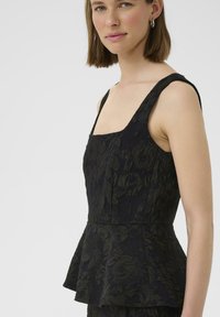 Haut peplum noir avec un décolleté carré, fabriqué à partir d'un tissu texturé arborant un motif floral ; bretelles larges et corps ajusté.