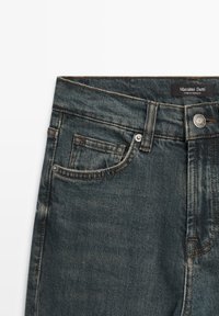 Jean en denim délavé foncé avec poches avant, rivets, passants pour ceinture, fermeture à bouton métallique, et une étiquette "Massimo Dutti" sur la ceinture.