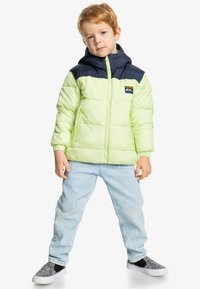 Světle zelená zateplená bunda s tmavě modrou horní částí a kapucí, zapínání na zip, nášivka s logem a ribbované manžety. Vytvořený outfit doplňují světlé modré džíny a boty se vzorem.