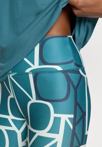 Τιρκουάζ αθλητικό κολάν με αφηρημένα λευκά και ναυτι κά γεωμετρικά σχέδια, με λεία υφή και εμφανείς ραφές.