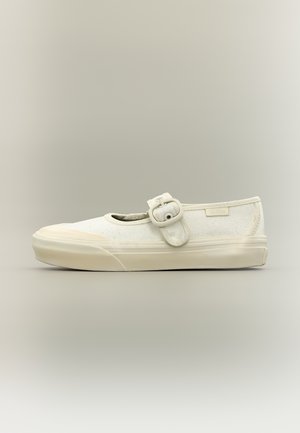 Zapatilla estilo Mary Jane de lona blanca con suela gruesa y correa ajustable con hebilla sobre un fondo neutro.