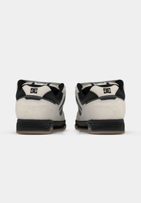 Gray suede sneakers with black accents, featuring a padded collar, a textured rubber sole, and a prominent logo on the back.