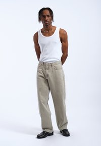Helle graue Jeans mit lockerer Passform, aus Denim gefertigt. Kombiniert mit einem weißen, gerippten Top und schwarzen Lederschuhen. Einfaches, sauberes Design.