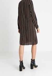 Svart och beige randig klänning med långa ärmar och rak skärning, kombinerad med blanka svarta ankelstövlar med en rejäl klack.