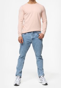 Chemise à manches longues rose clair associée à un jean bleu clair et des baskets blanches. La chemise présente un col rond et une coupe ajustée.