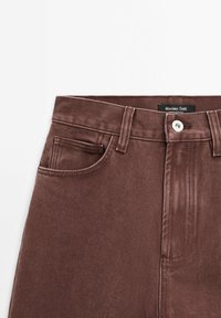 Jean en denim marron avec poche avant, passants pour ceinture, bouton argenté et étiquette Massimo Dutti à la taille.