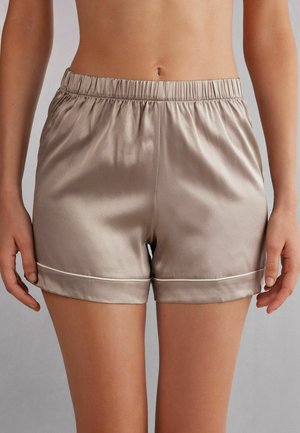 Satinshorts med elastisk midja, beige färg, uppvikt fåll med vit piping och en mjuk yta.