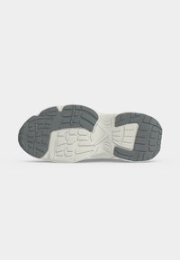 Semelle d'une chaussure de sport avec un profil en caoutchouc gris et blanc conçu pour l'adhérence et la durabilité, montrée sur un fond clair uni.