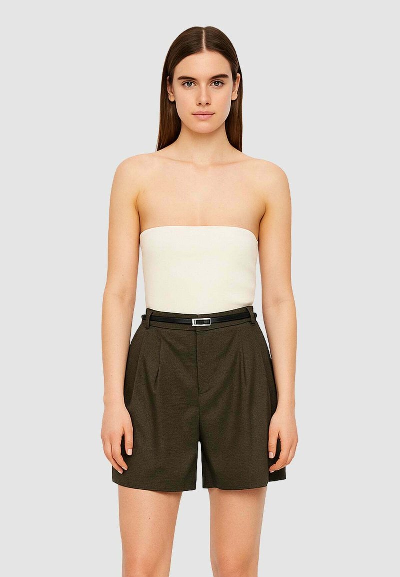 Top crema senza spalline abbinato a pantaloni corti scuri a vita alta, caratterizzati da una cintura nera. Tessuto liscio con dettagli a pieghe.