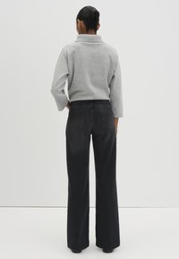 Pull en maille gris avec un col haut, associé à un jean noir à taille haute et jambes larges avec des poches arrière.