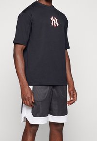 Svart bomullströja med en vit och röd New York-logotyp på bröstet, kombinerad med svarta meshshorts med vita detaljer och en sportig design.