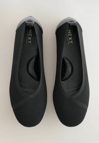 Schwarze Ballerinas zum Hineinschlüpfen aus strukturiertem Strickmaterial, mit glatter Lackleder-Spitze und gepolstertem Fußbett mit Punktmuster.