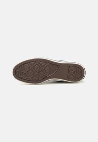 Suela de zapatilla de goma marrón con un patrón de agarre texturizado y acentos elevados. Murales laterales de color claro y marca clásica de Converse.