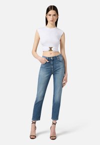 Top corto bianco con una fibbia dorata, abbinato a jeans dritti azzurri chiari e tacchi neri con cinturini. Tessuto liscio e vestibilità su misura.