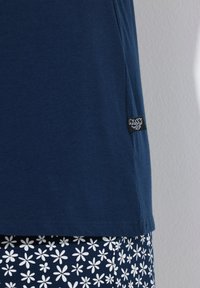 Marineblauwe katoenen t-shirt met een gladde structuur, voorzien van een zijlabel. Gecombineerd met witte stof met een bloemmotief aan de onderzijde.