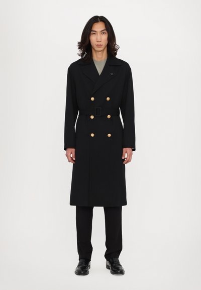 Black double-breasted coat with gold buttons, belted waist, and notched collar. Suit trousers and black shoes complete the look.